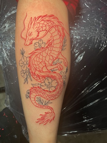 Red Haku Dragon With Blue Cherry Blossoms Fine Line Tattoo By Lyric TheArtist At Iron Palm Tattoos. The cherry blossom is known for its fleeting nature, as the blossoms only last for a short time before falling from the tree. This represent the transience of life and also rebirth and renewal. When combined with a red Haku the tattoo symbolized the wearer's resilience and ability to bounce back from adversity. We're open late night until 2AM most nights. Call 404-973-7828 ot stop by for a free consultation with Lyric or any other Iron Palm body artist. Walk Ins are welcome.