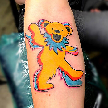Grateful Dead Dancing Yellow Bear Tattoo By Khem At Iron Palm Tattoos in Atlanta, GA. The bears were originally created by artist Bob Thomas as part of the back cover artwork for the band's 1973 album titled "History of the Grateful Dead, Volume One (Bear's Choice)." The bears were intended to represent each member of the band in a whimsical and lighthearted way. Over time, the dancing bears gained popularity and became closely associated with the Grateful Dead's music and culture. Call 404-973-7828 or stop by for a free consultation with Khem. Walk Ins are welcome.