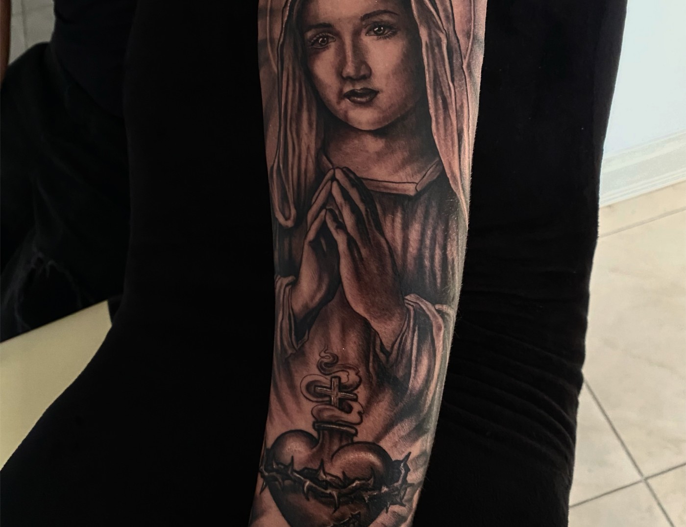 Madonna Blessing Hearts Black & Gray Photo Realism Portrait Tattoo By Rene Cristobal, A Guest Artist At Iron Palm Tattoos. The Madonna is a representation of Mary praying. The word "Madonna" comes from the Italian "ma donna," which means "my lady". Although usually depicted with baby Jesus it is also popular to see Mary praying or blessing something. Rene comes to us from Vision tattoo studio in Concepcion, Chile and is available for booking Sep 11th - Sept 18th 2023. We're open late night until 2AM. Call 404-973-7828 or stop by for a free consultation. Walk Ins are welcome.