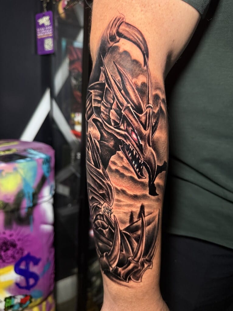 Black and gray dragon forearm tattoo with horns, claws, storm clouds, and glowing eye detail