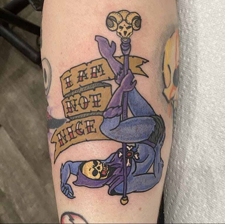 A colorful Traditional tattoo featuring Skeletor holding his staff beneath a bold “I AM NOT NICE” banner. Strong black outlines, saturated purple and gold tones, and a playful character design give the piece a classic animated feel. Tattooed by Tupicalo at Iron Palm Tattoos & Body Piercings in downtown Atlanta, GA. Call or text 404-973-7828. Tattoo consultations are free and walk ins are always welcome.